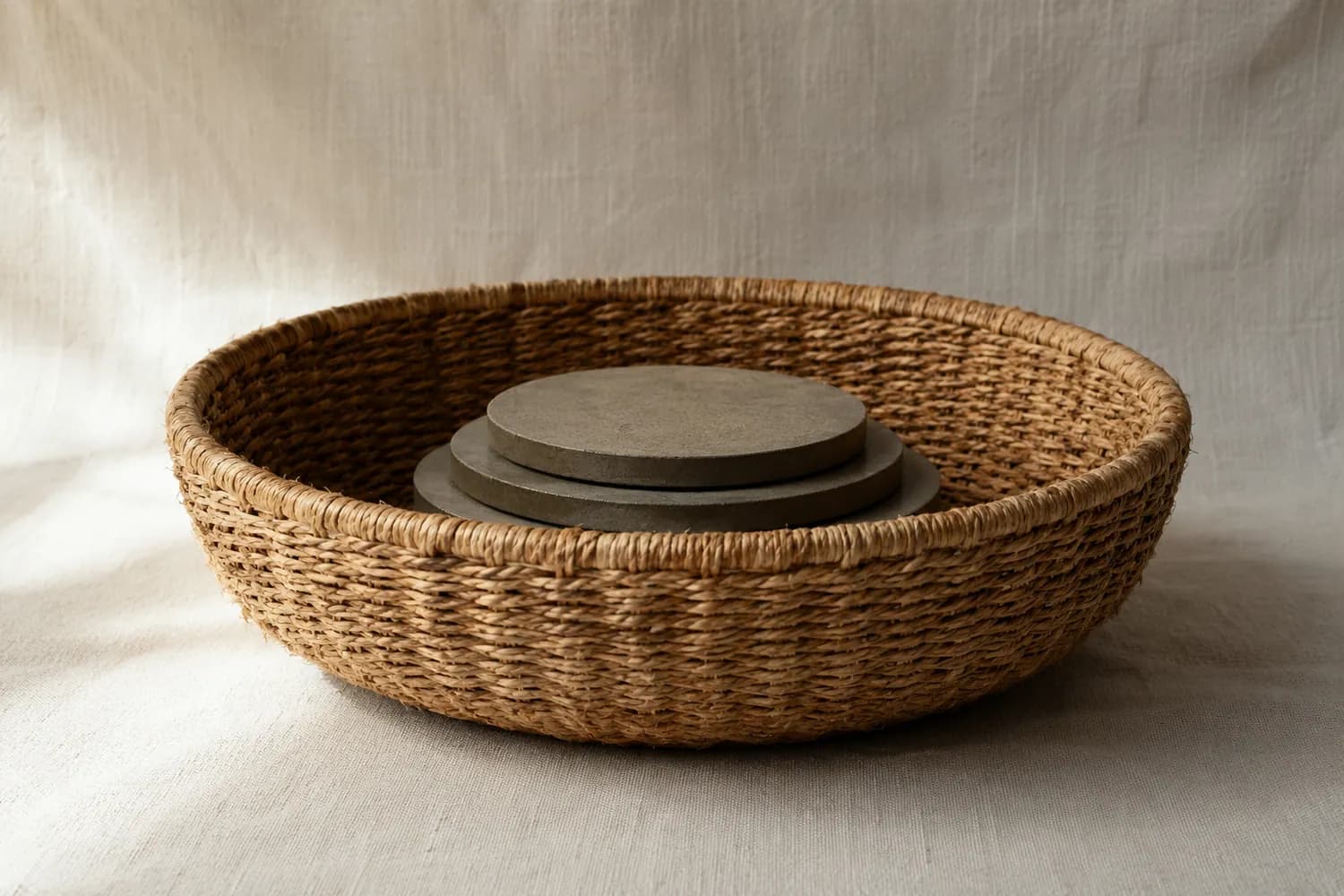An empty round basket on a plain surface with flat calibration weights resting evenly across its base, photographed from the side.